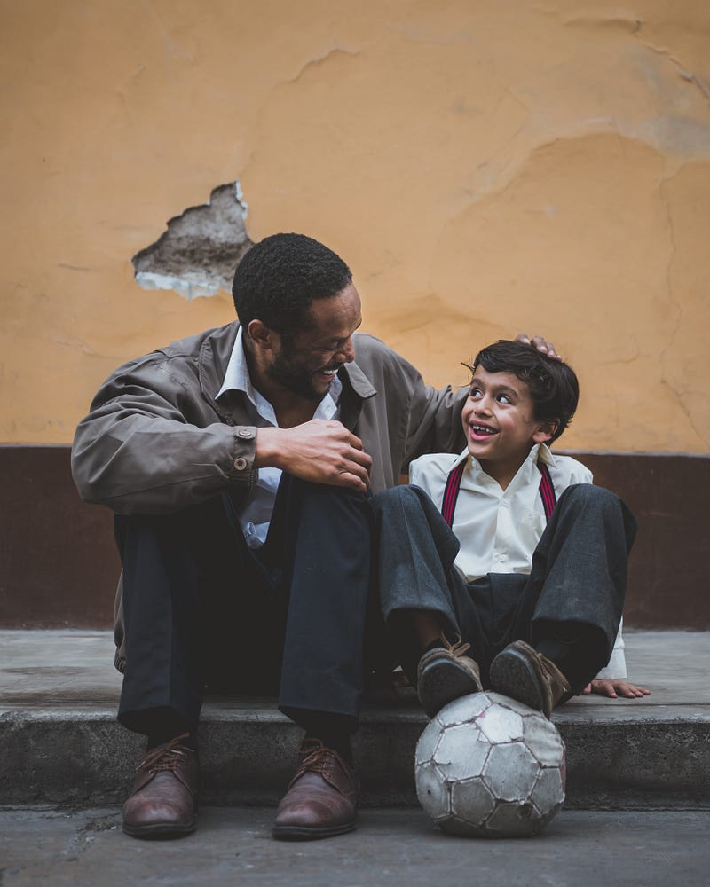 Father sitting next to his smiling son with a footbal below his feet